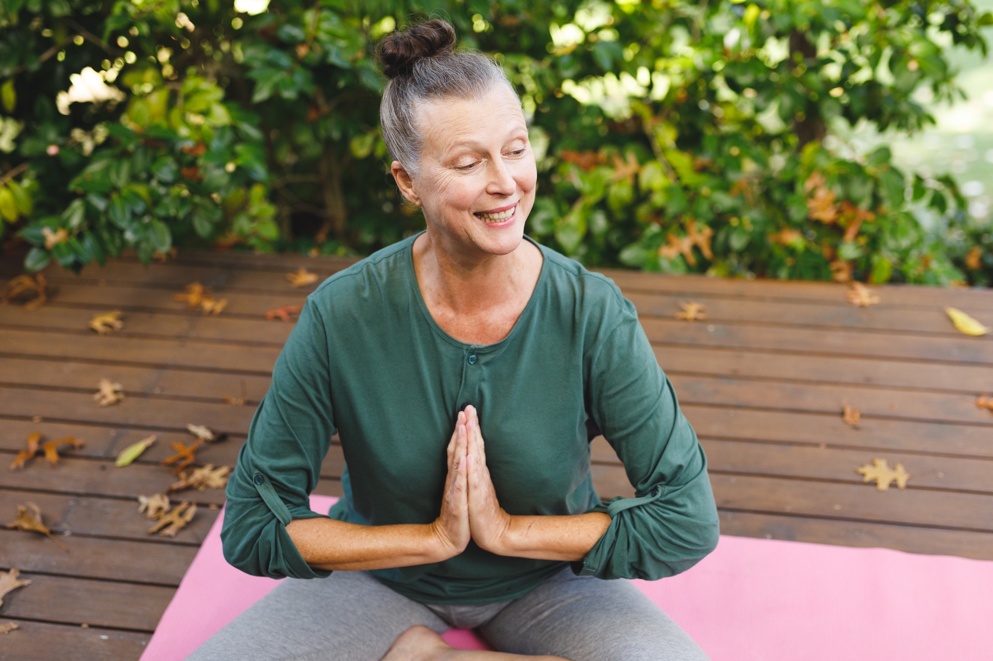 Happy senior caucasian woman practicing yoga, meditating in sunny garden